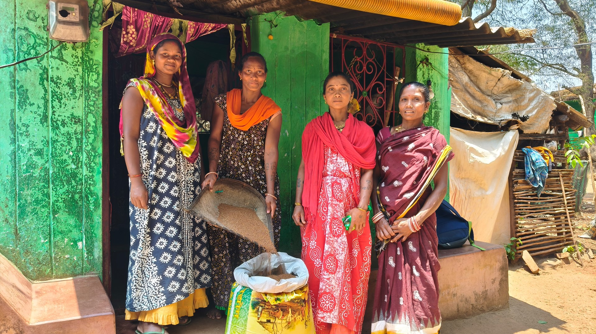 4 tribal women standing in front of a seed bank showing the seeds they have grown and collected
