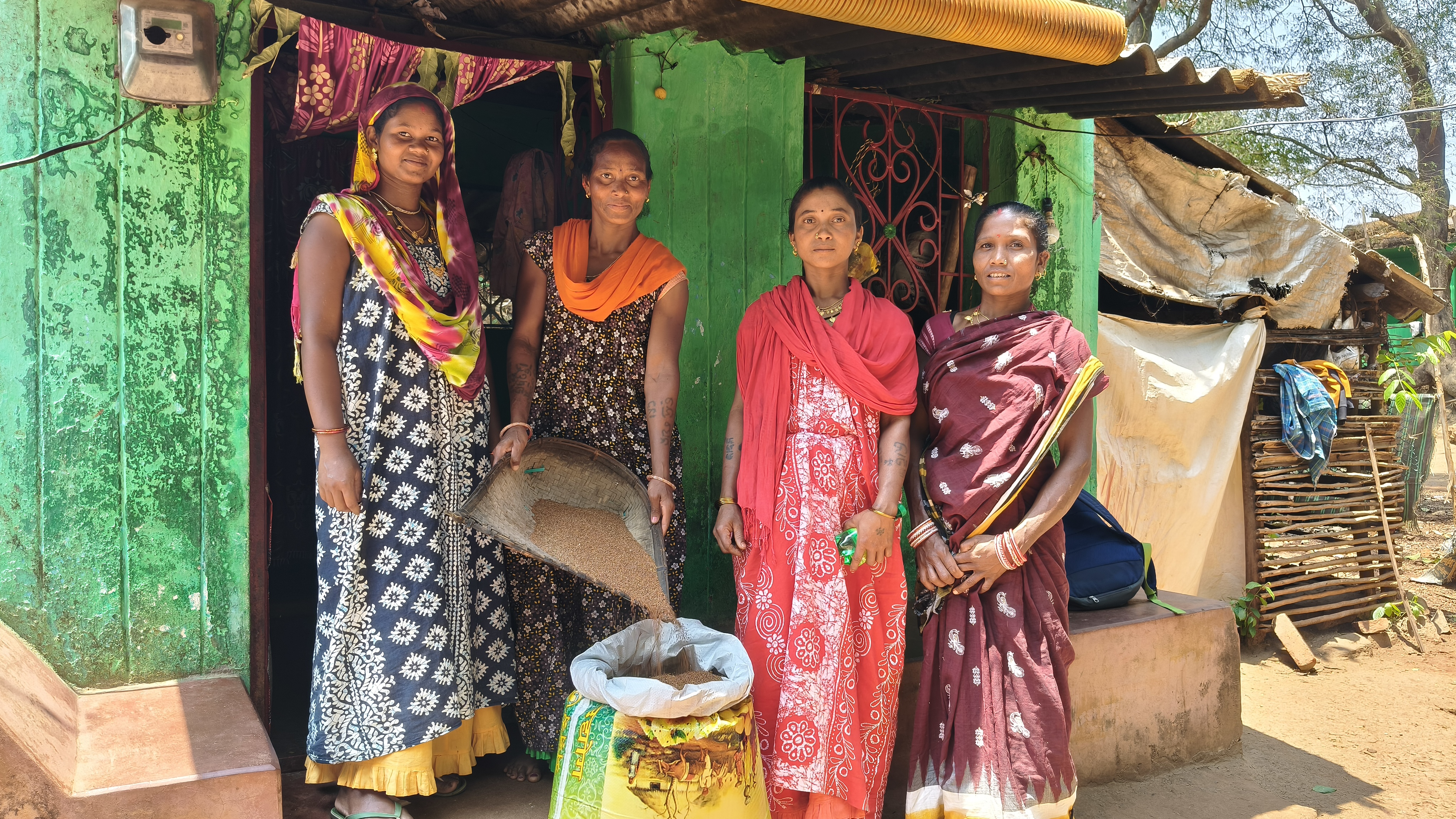 Four women in colourful clothes standing in front of a seed bank with a huge bag of seeds in front of them