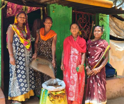 4 tribal women standing in front of a seed bank showing the seeds they have grown and collected